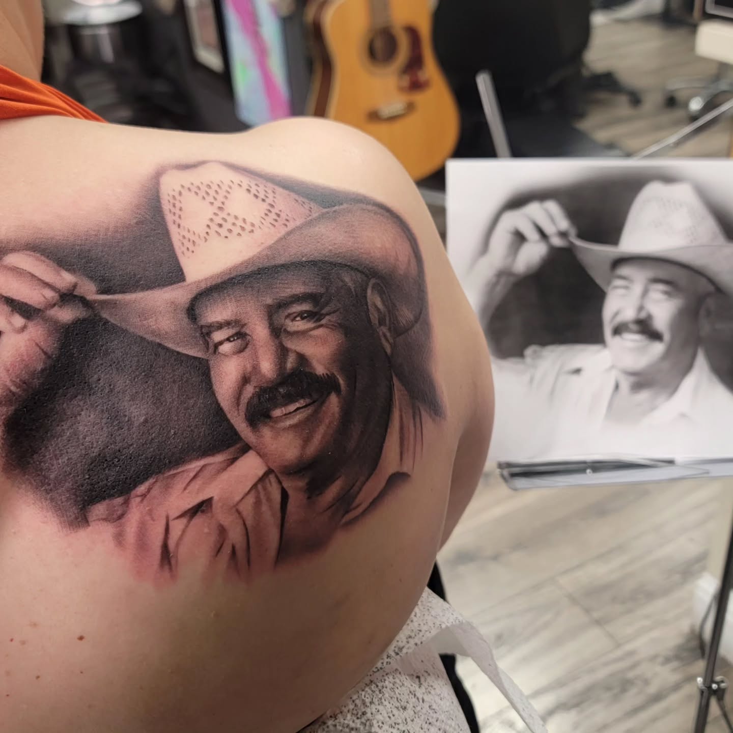 Black-and-grey cowboy portrait tattoo beside its photo reference