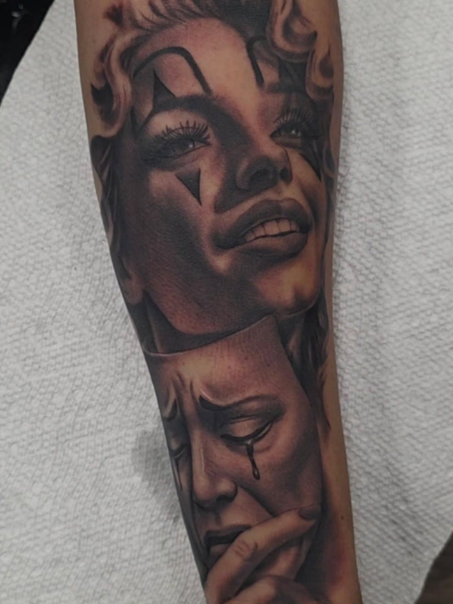 Black-and-grey forearm tattoo of masked women making a hush gesture