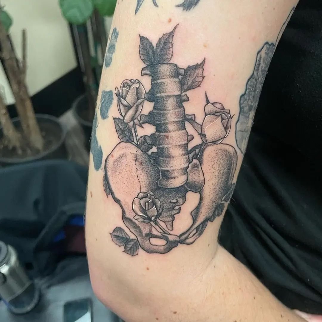 Black-and-grey anatomical pelvis and roses upper-arm tattoo