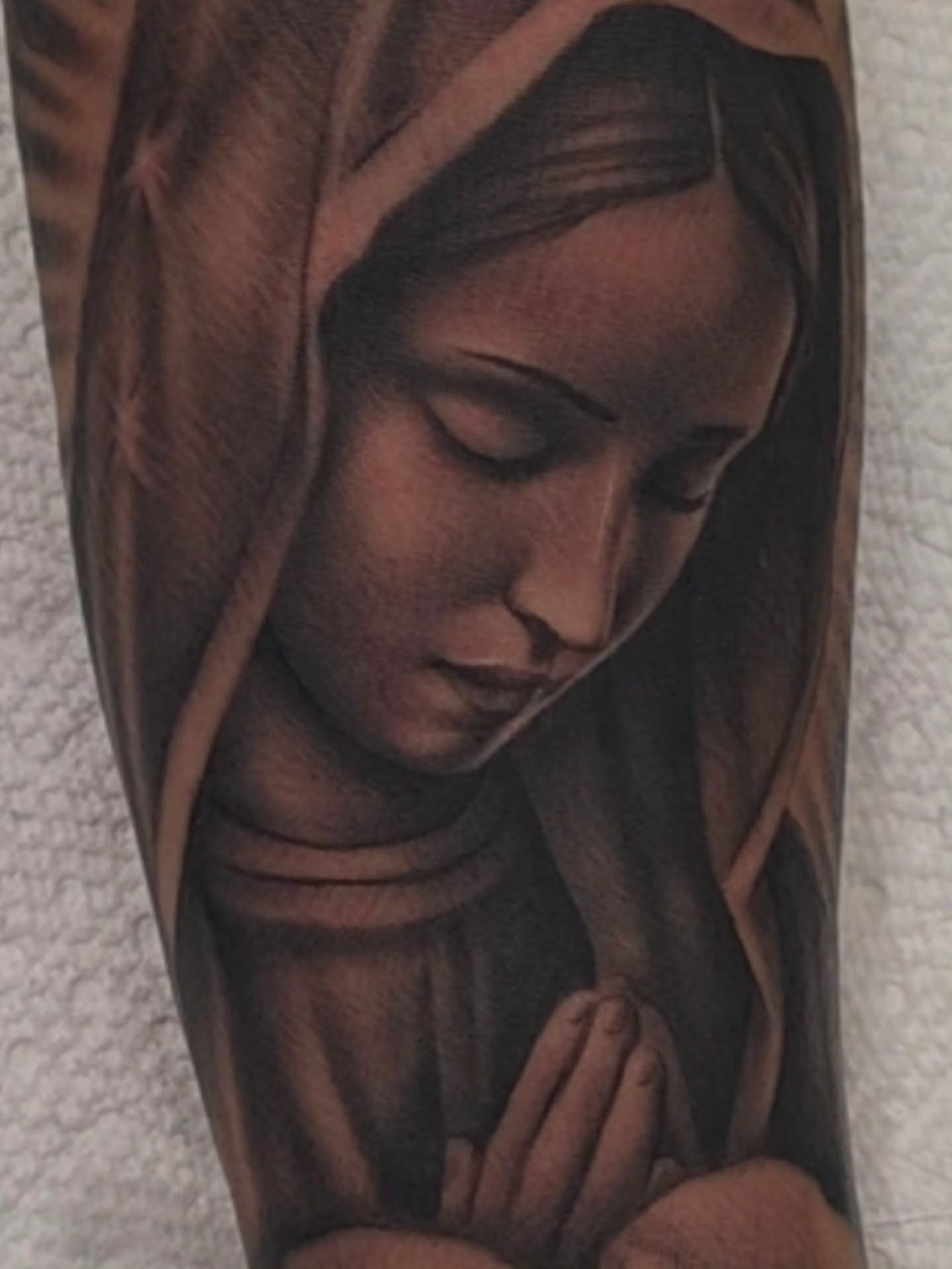 Close view of a black-and-grey praying Mary portrait tattoo