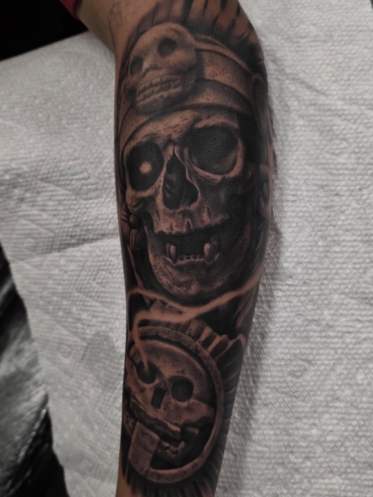 Black-and-grey skulls and mechanical elements forearm tattoo