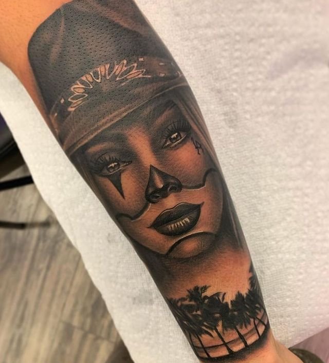 Black-and-grey clown portrait forearm tattoo with palm trees